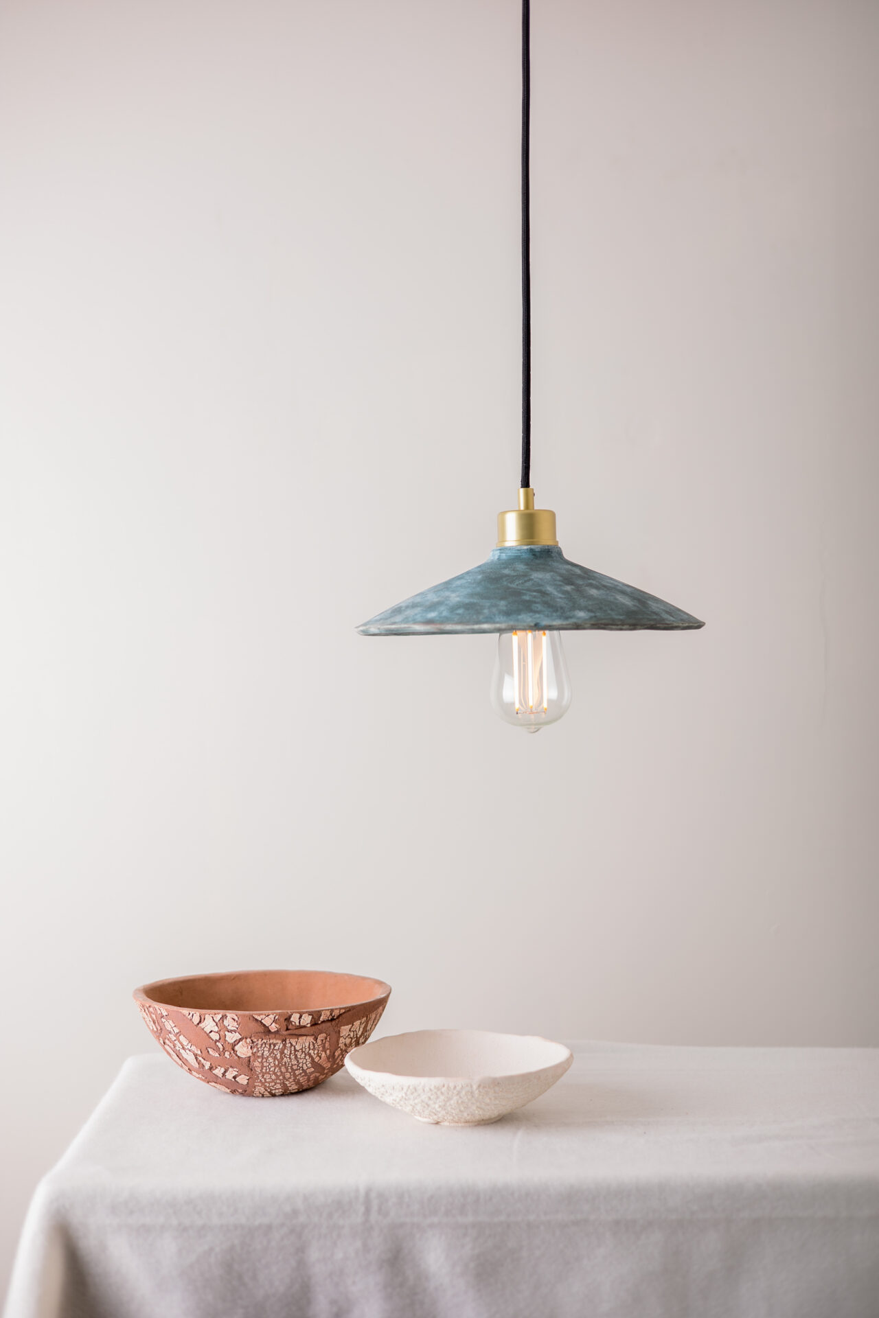 Ceramic light that hangs on the white table over two ceramic bowls