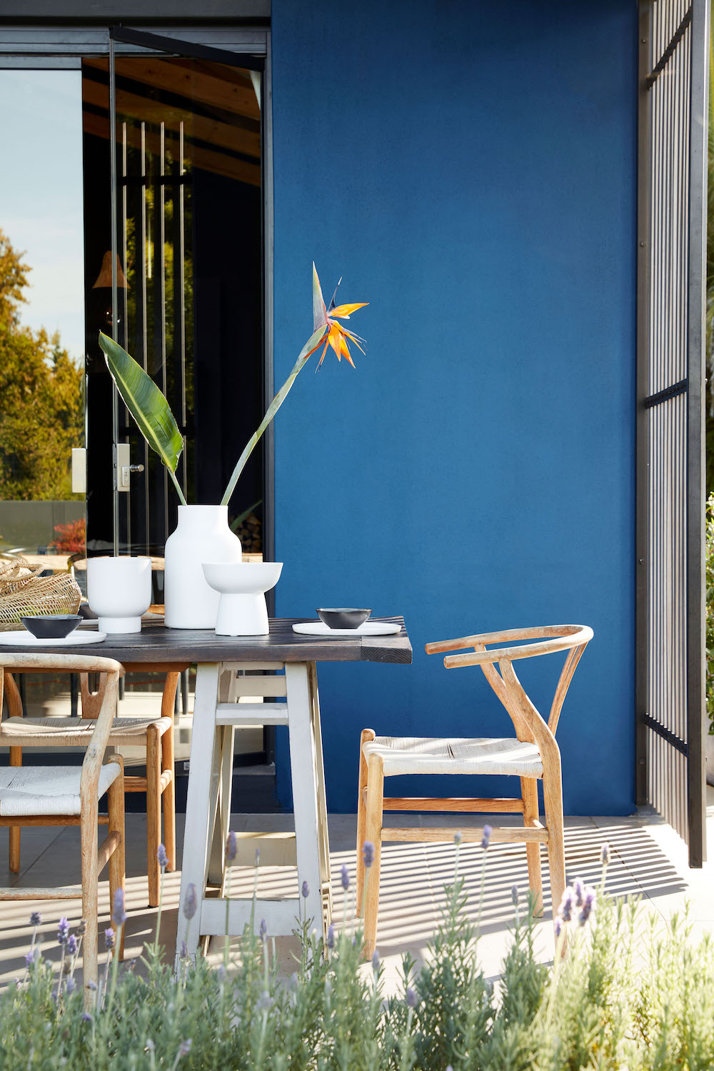 Little Greene intelligent outer walls in an electric blue that is used for an outdoor dining area. There is a black and white table with wooden chairs that are located around it.