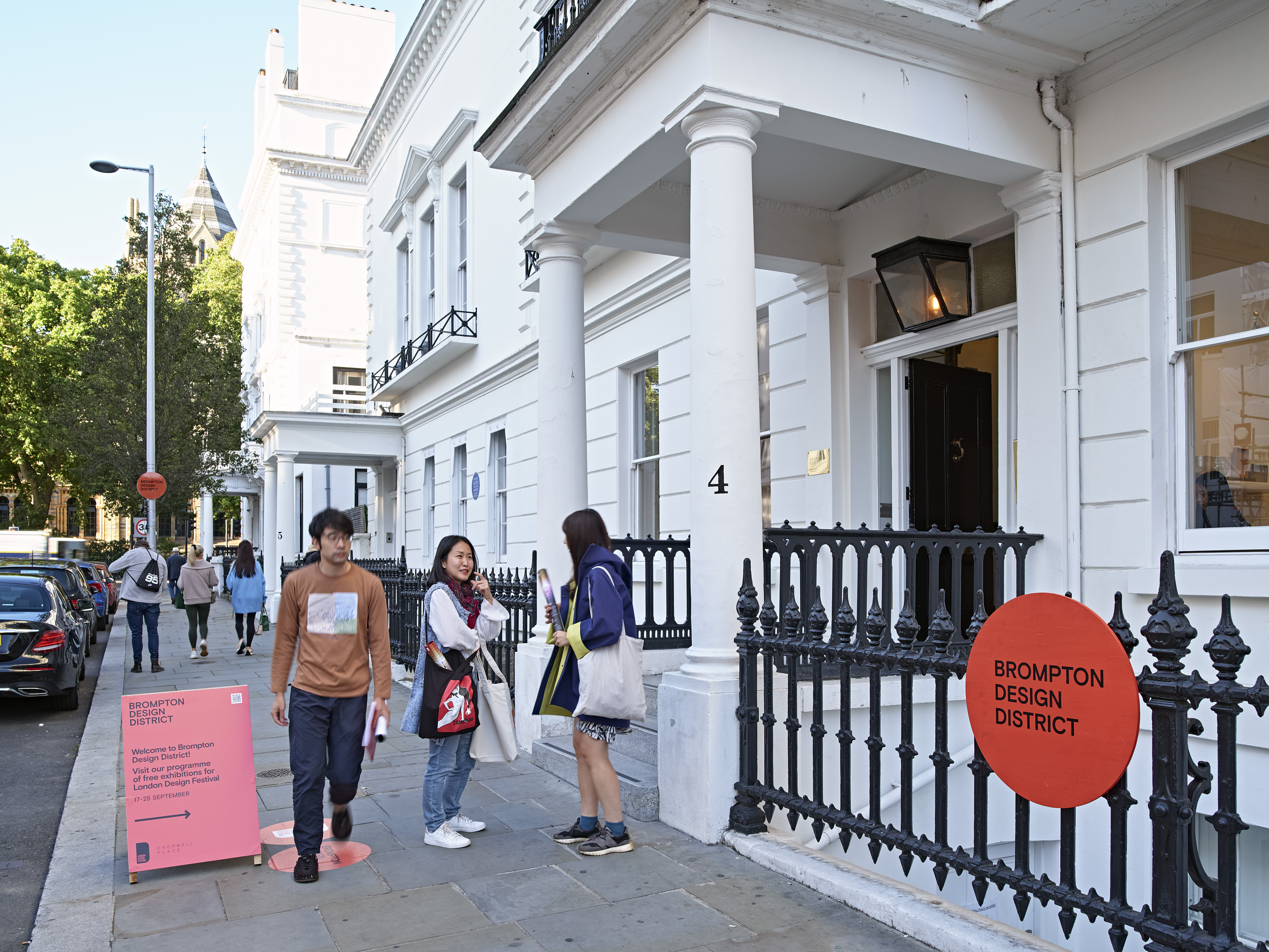 People who go and stand next to the entrance of a white building in a street in West London
