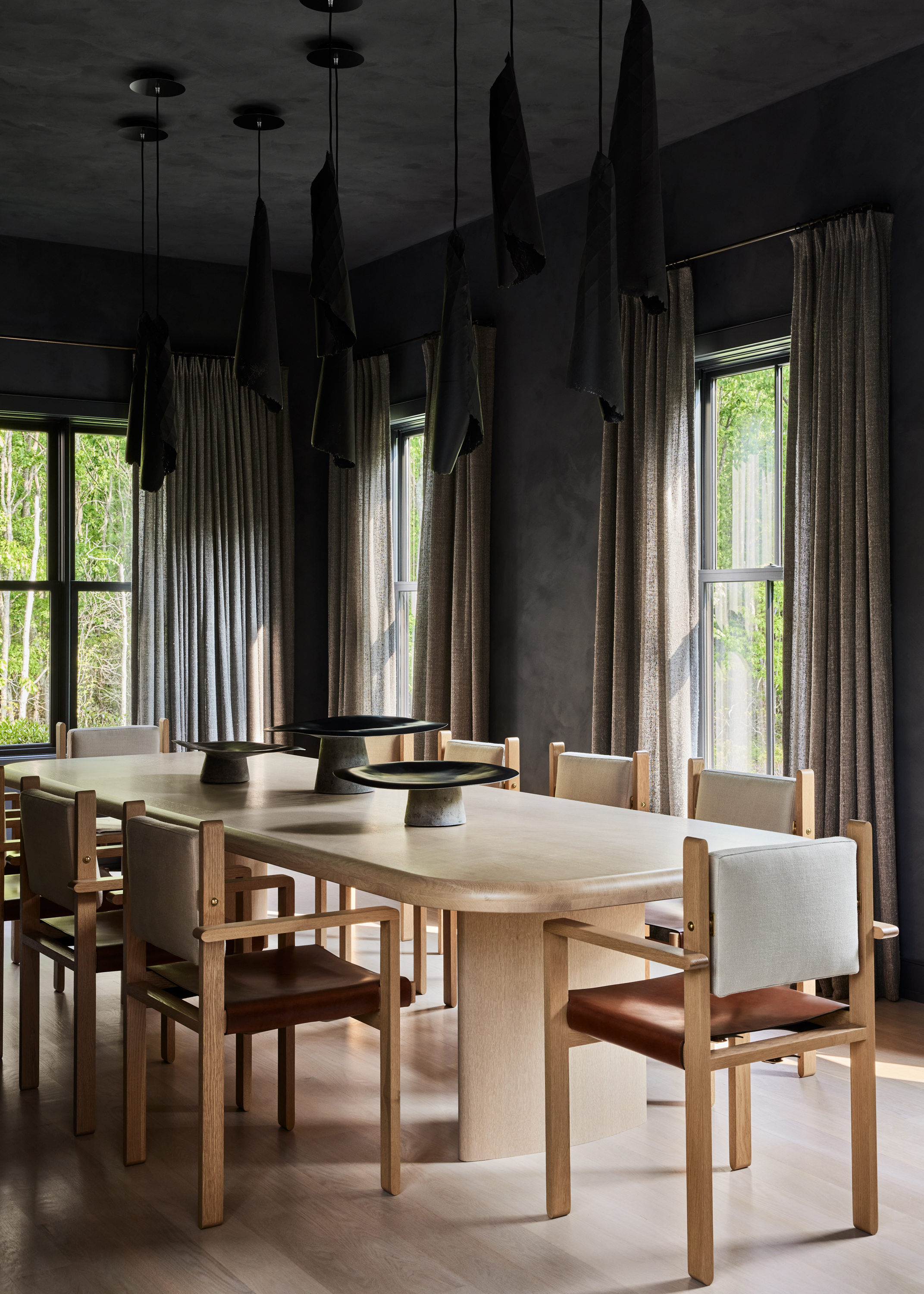 A dark gray dining room with well -stared curtains. There is a light wooden dining table with wood and leather dining chairs.