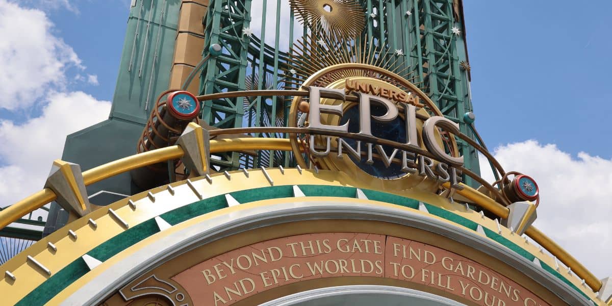 Large decorative entrance sign for the universal epic universe with golden and green accents, a sunburst design, gears and the words: 