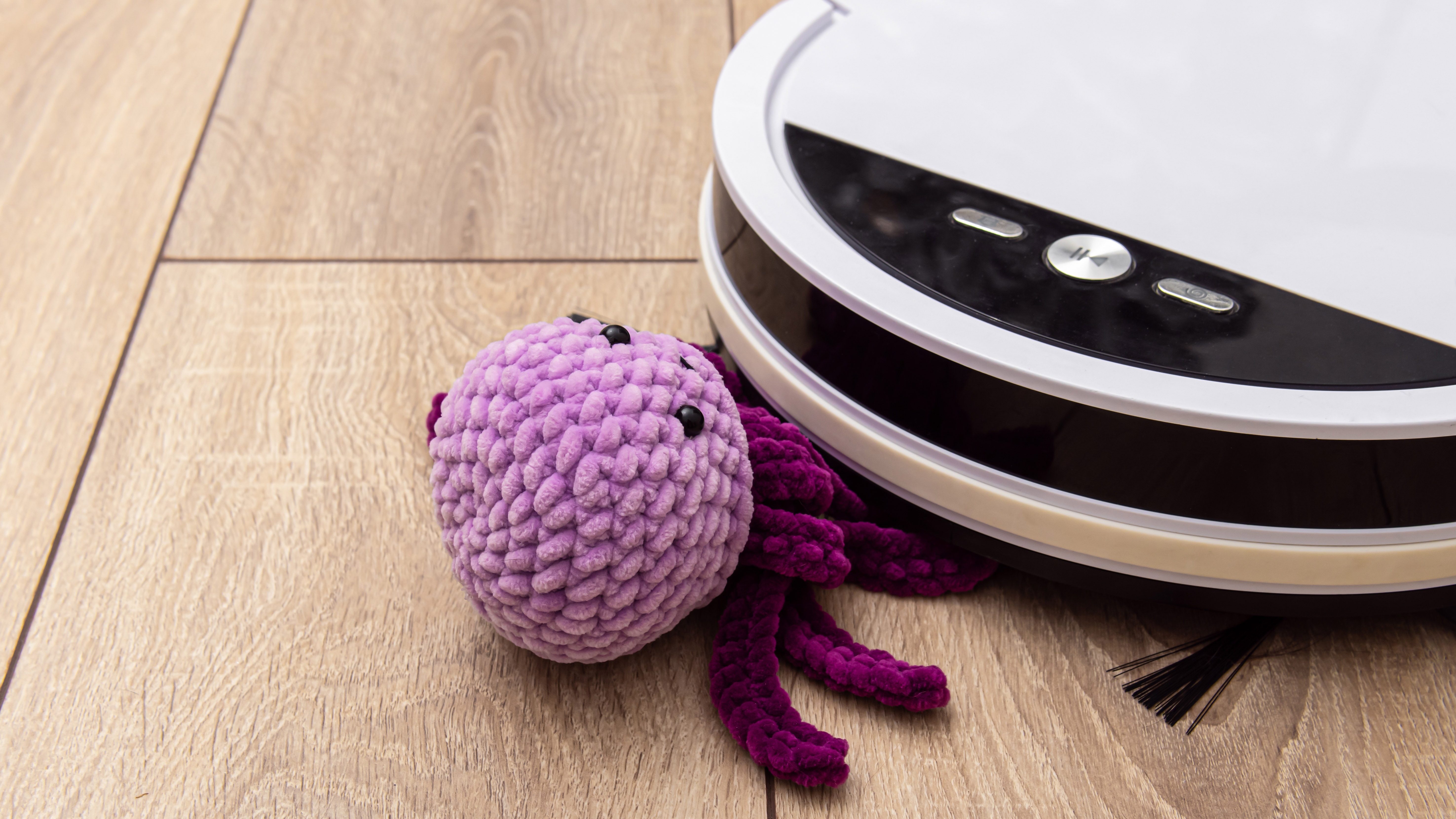 Purple toy is under white robot vacuum cleaner