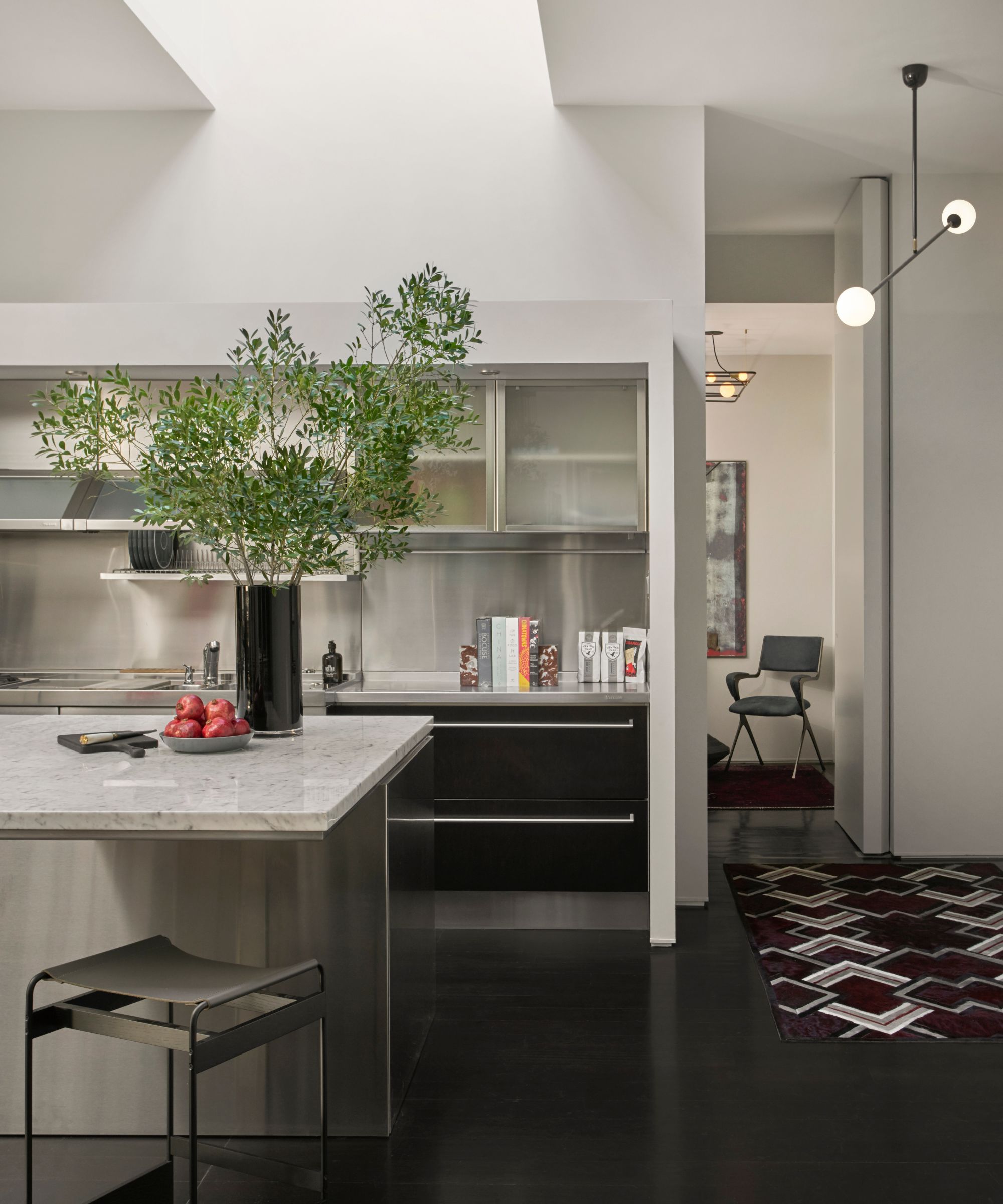 A kitchen with stainless steel worktops, an island with stone worktops and black cupboards