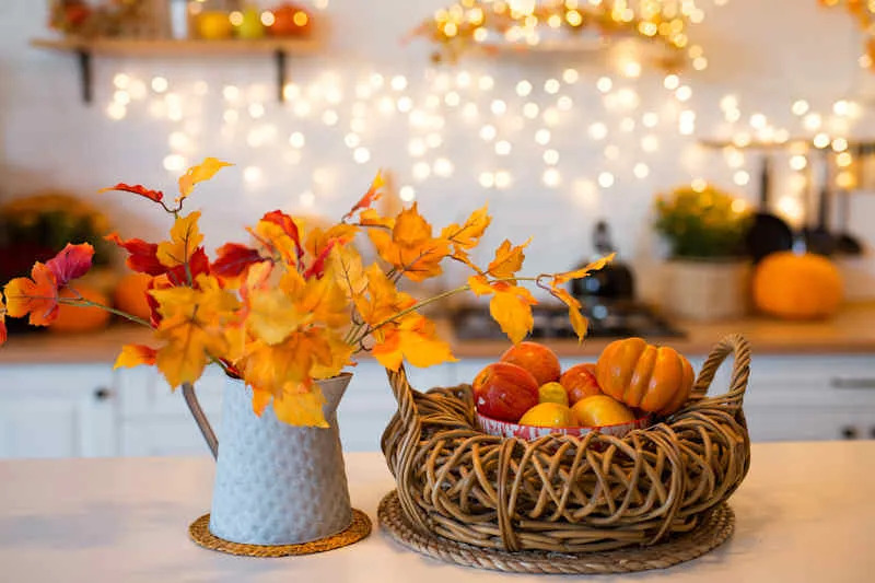 Autumn kitchen. Red and yellow leaves and flowers in the vase and pumpkin on a light background