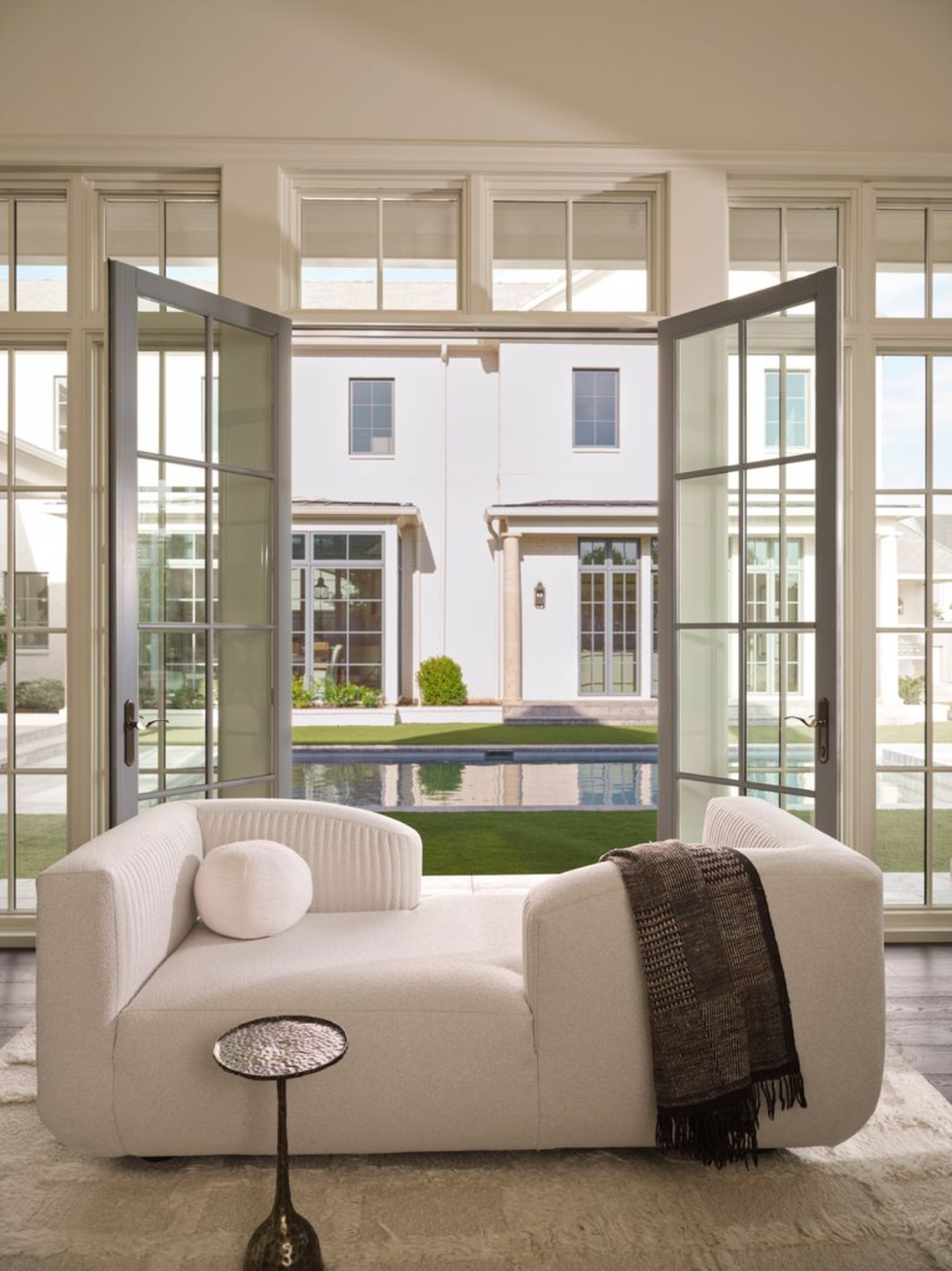 Light room with white sofa, open doors and a view of the pool and the modern house outside.