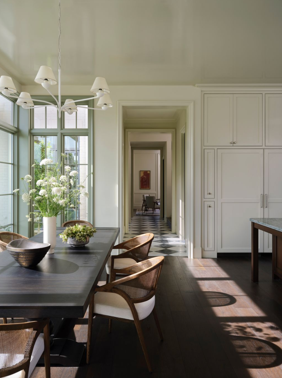 Elegant dining area with large windows, dark table, chairs and chandeliers that leads to a hallway.