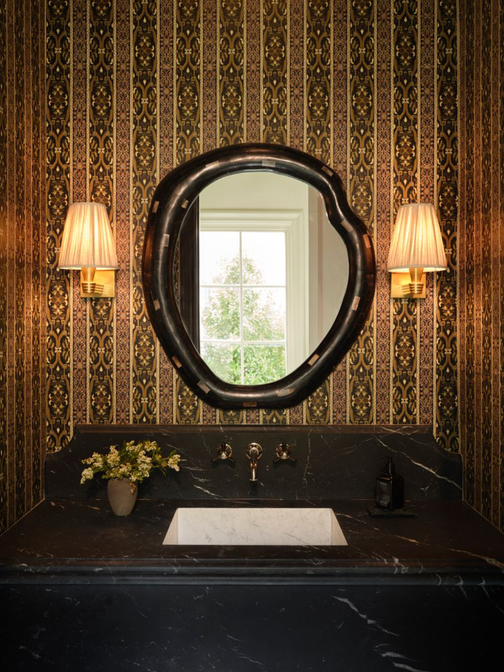Elegant bathroom with decorated wallpaper, unique mirror and wall lights over a black sink.