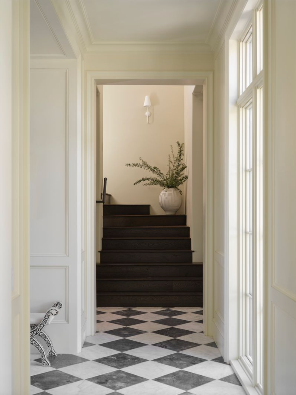 Hall with a checked floor, dark steps, potted plants and wall lights.