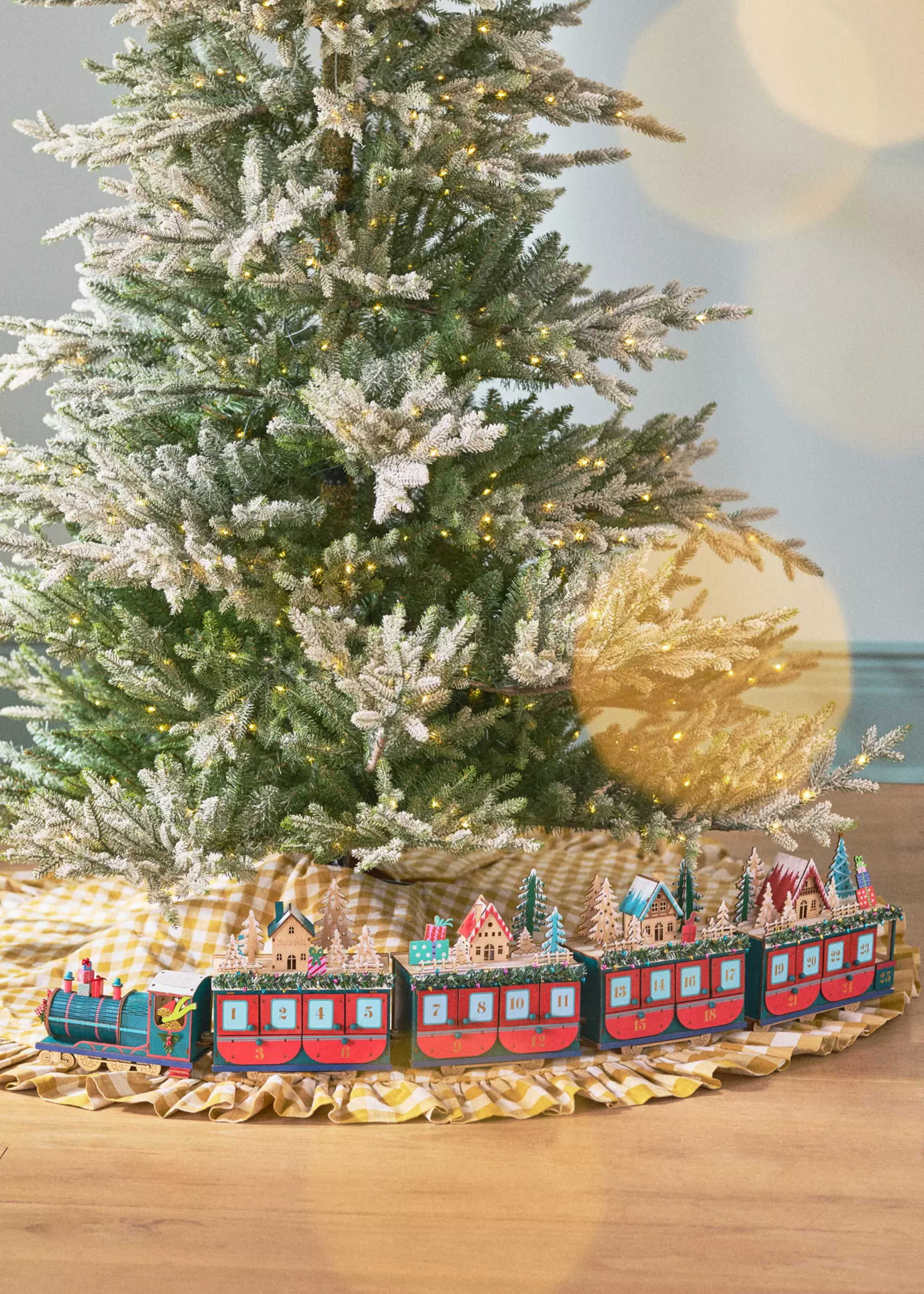 The anthropology -train -Advent calendar, which has placed around the Gingham rock of a frosted Christmas tree with red cars with trees and Christmas houses and a blue front car