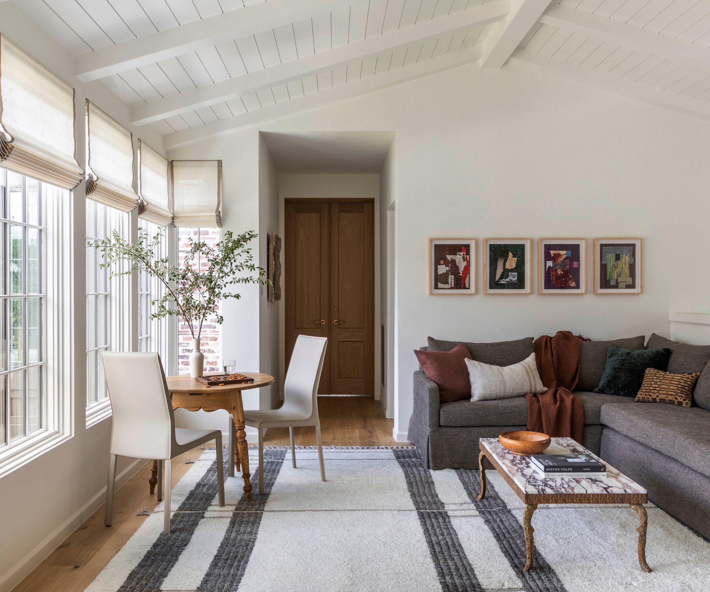 Open plan winter garden with a round wood-dining table, white chairs, gray sectensofa and a gallery wall
