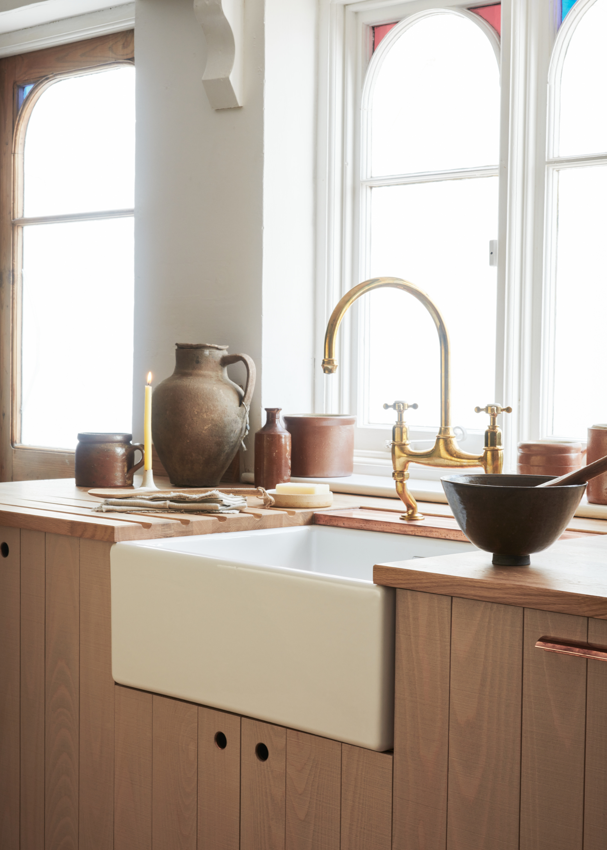 Sink area in a wooden kitchen surrounded by ceramics. The tap is gold and has a marble insert