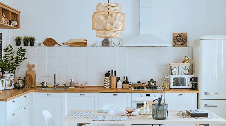 A modern white kitchen has depth due to warm wood, a striking lamp and accessories