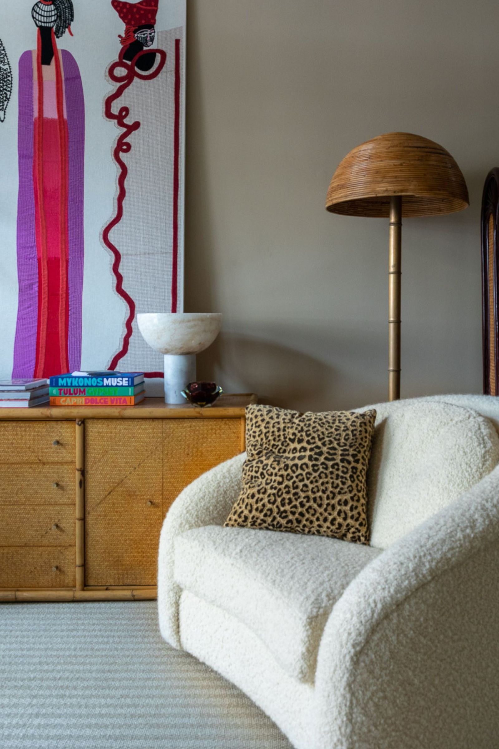 Boucle chair next to a wooden sideboard with great art and a rattan base lamp