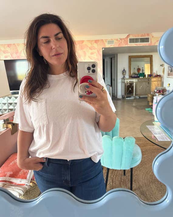 Katie Sturino takes a mirror selfie while wearing a white t -shirt at home.