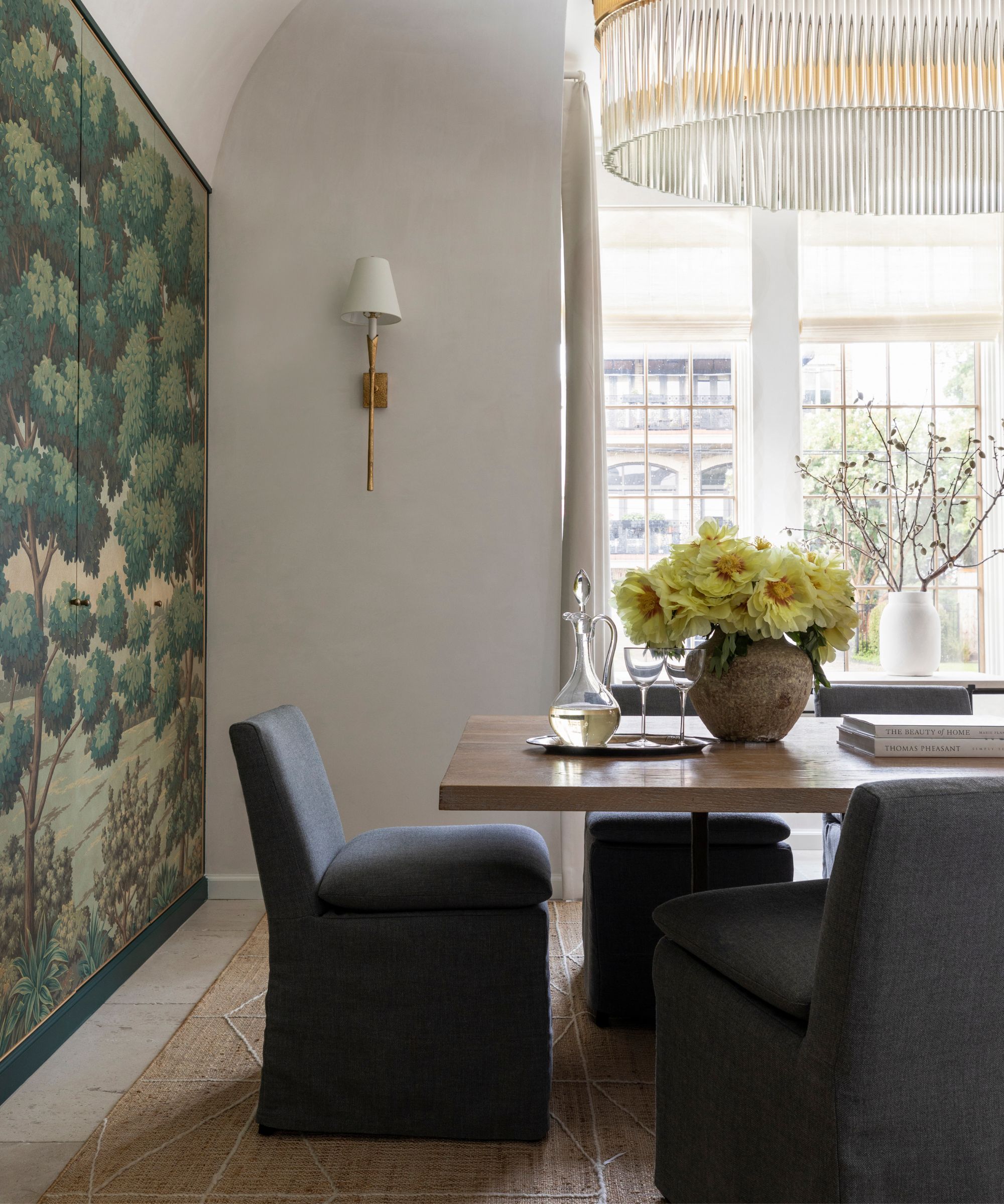 White painted dining room with large gold and crystal candlestick with wooden table, dark blue covered esühle with a large wall carpet