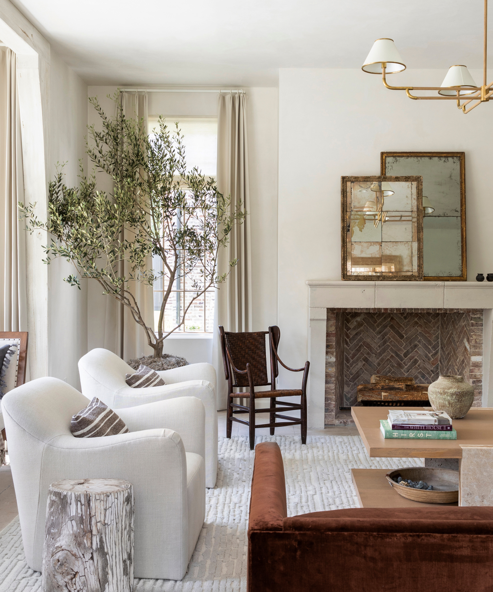 A neutral living room with a large tree, white armchairs and a fireplace.