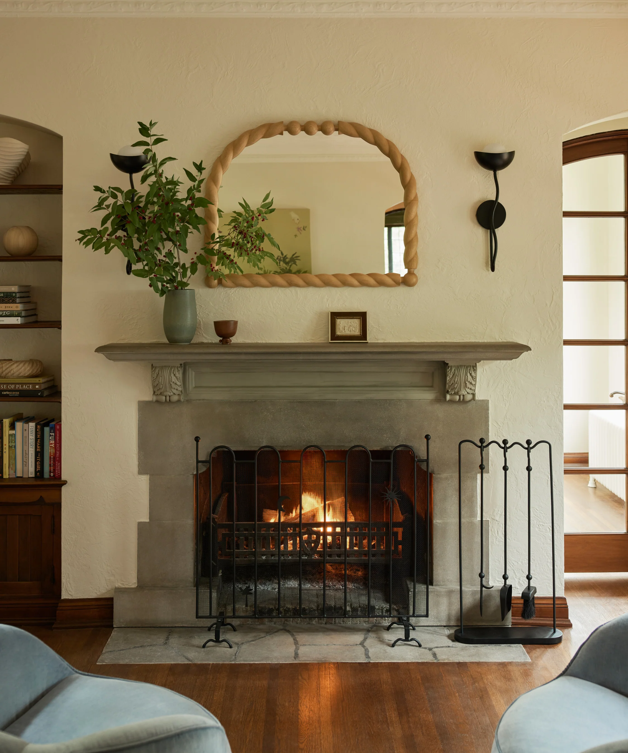 A living room with a stone fireplace, a metal fireplace, a wooden mirror and a plant in a vase on the fireplace
