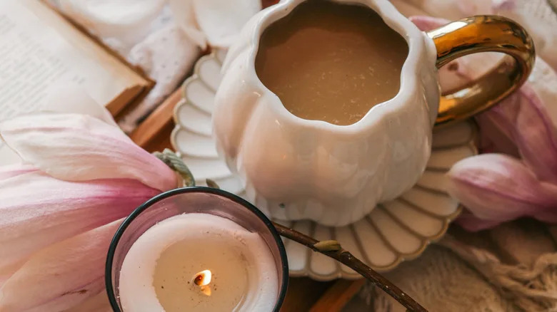 A teacup on a broken sauce next to a book, a candle and a real flower.