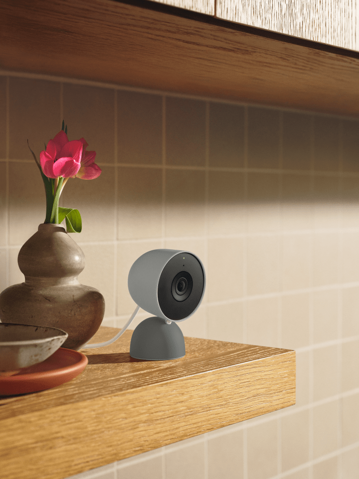 A gray surveillance camera on a wooden shelf next to a vase with red tulips.