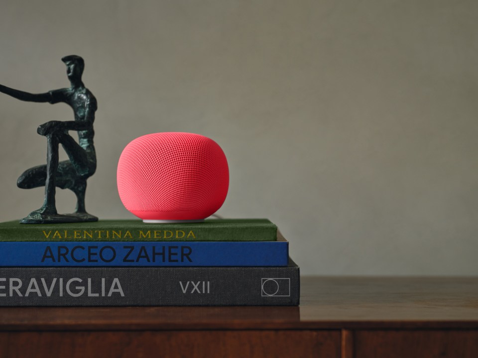 A red apple -home -mini sits on a stack of books next to a bronze figure.
