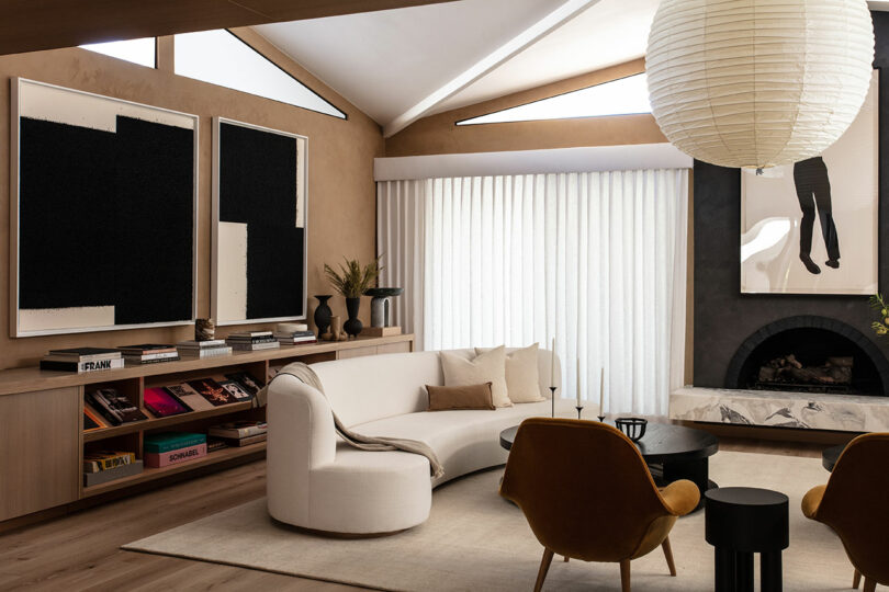 Modern living room with a curved white sofa, two mustard temperatures, black round coffee table, paper lantern, neutral decor, bookshelves and abstract art on the walls.