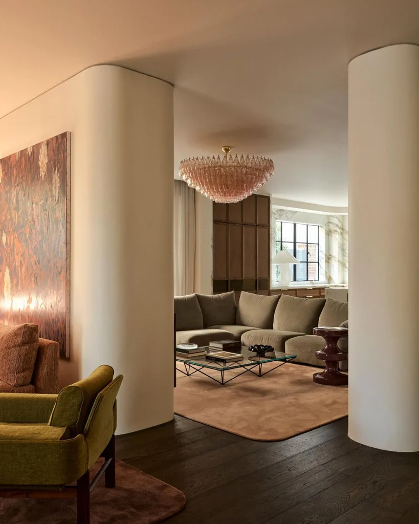 Glamorous living room with gray plush sofa, pink glass kron chandelier and curved white walls. 