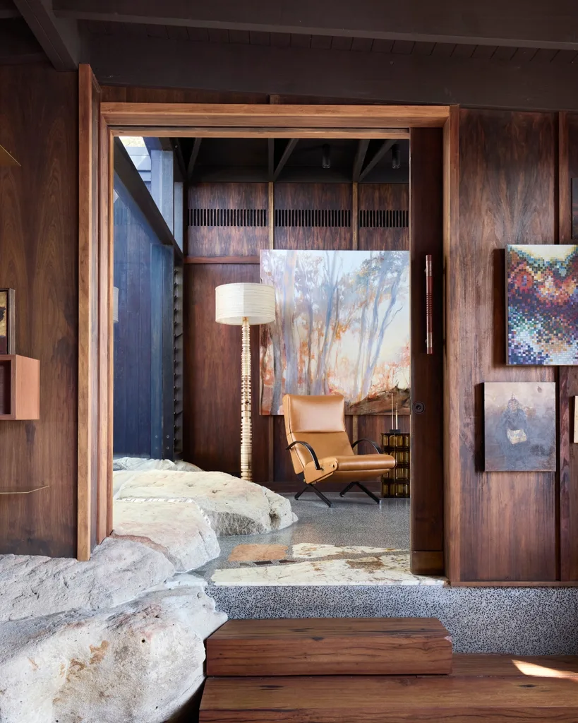 Interior with wooden walls, large stones, leather armchairs, floor lamp and works of art. 