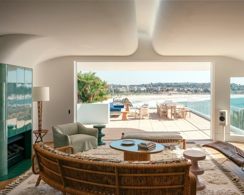 Coastal living room with a view of the beach, rattan sofa, green tiled retro fireplace and a lot of natural light. 