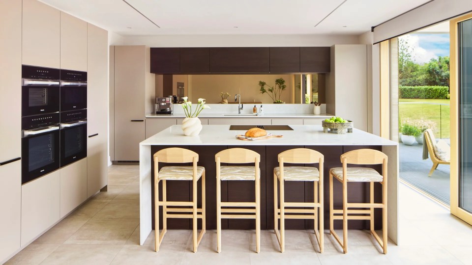 Modern kitchen with bright cabinets, built-in ovens, an island with seating and a large sliding glass door leading to the garden.