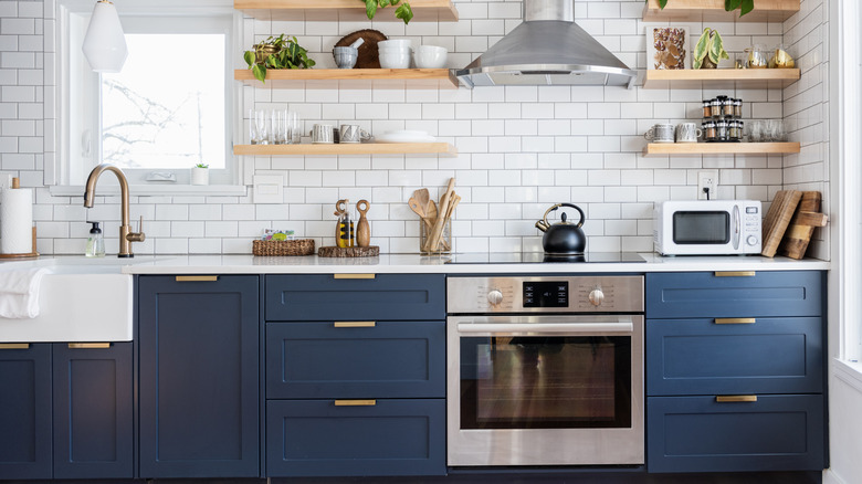A kitchen with dark blue cabinets, wooden shelves and white countertops