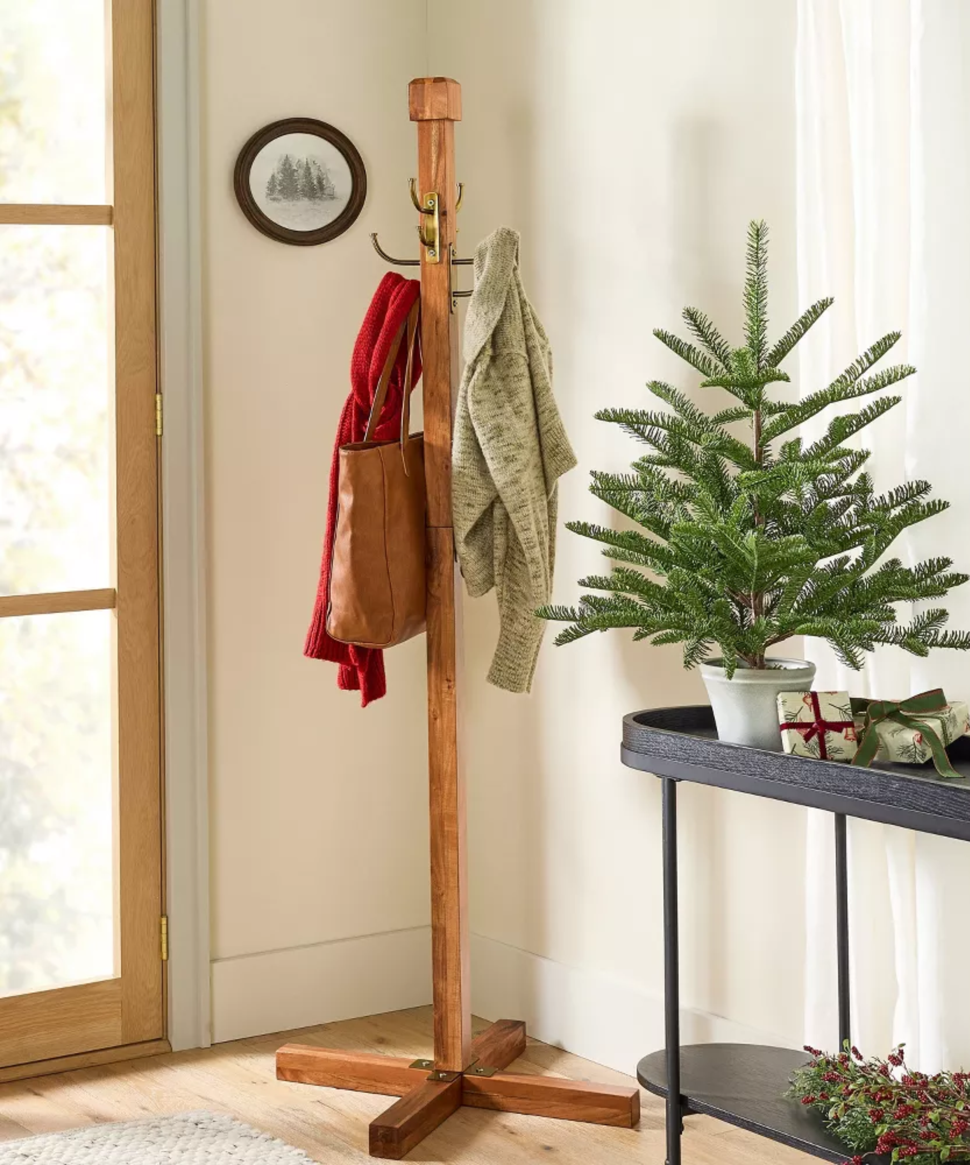 an entryway with a wooden coat rack with two coats and a bag and a small black table with a small tree and two wrapped gifts