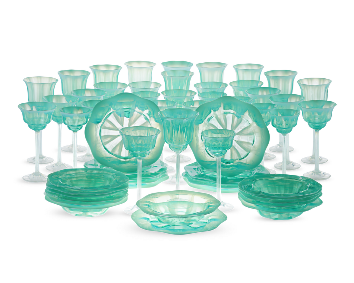 Teal vintage glass dinnerware set with plates and glasses arranged on a reflective surface against a black background.