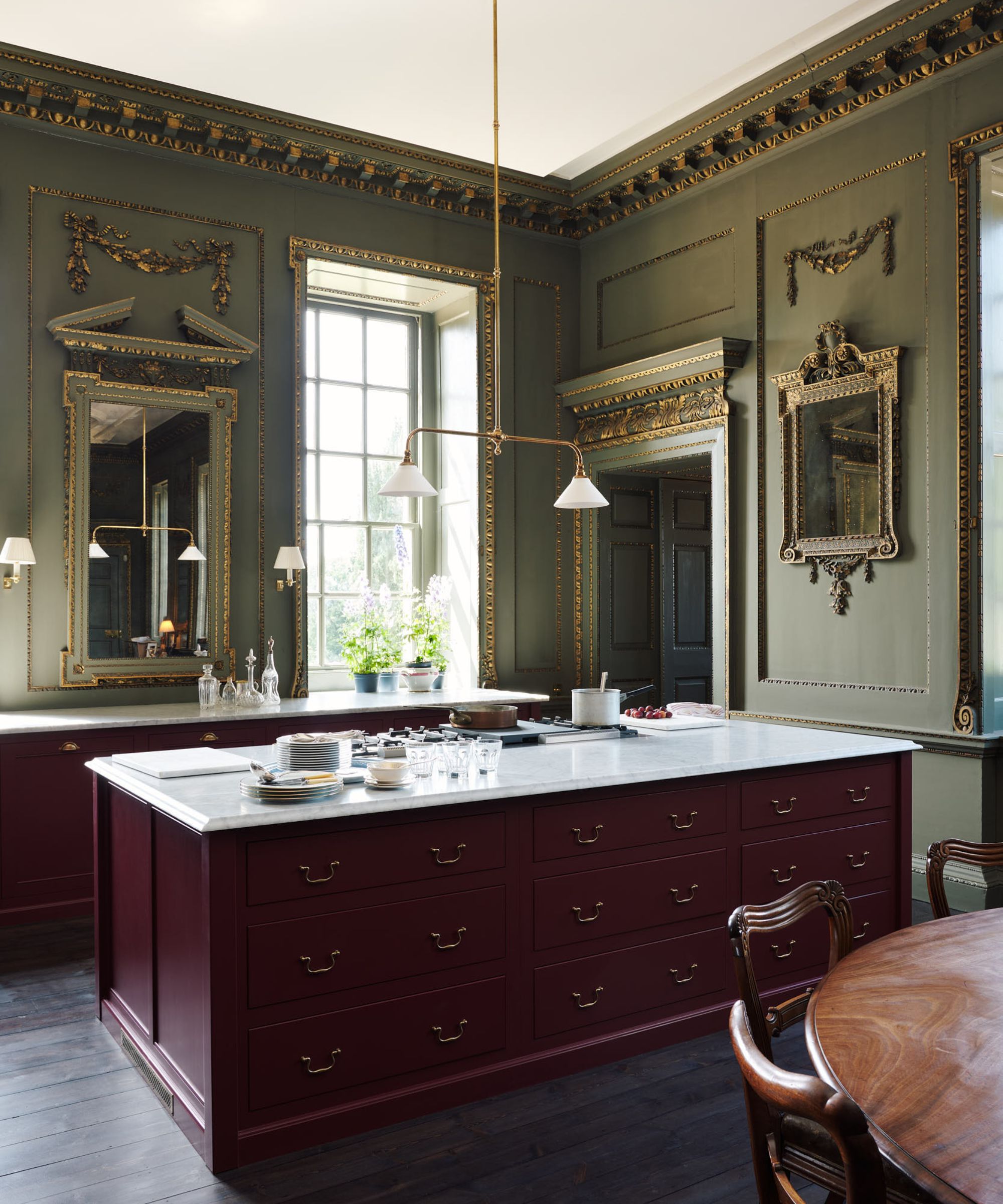 A stately eat-in kitchen with green walls, red cabinets, ornate mirrors and marble countertops
