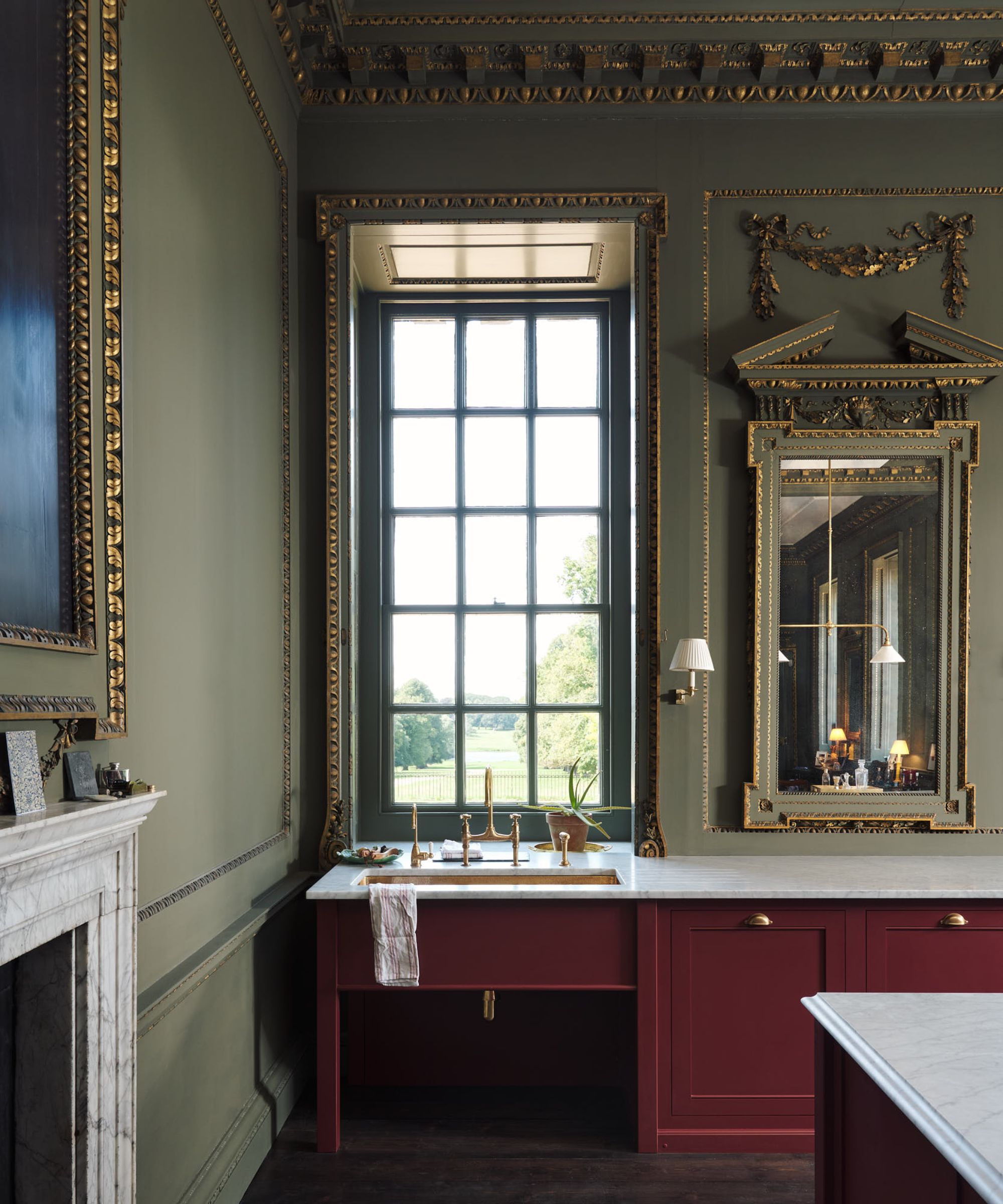 A stately eat-in kitchen with green walls, red cabinets, marble countertops and mirrors on the walls