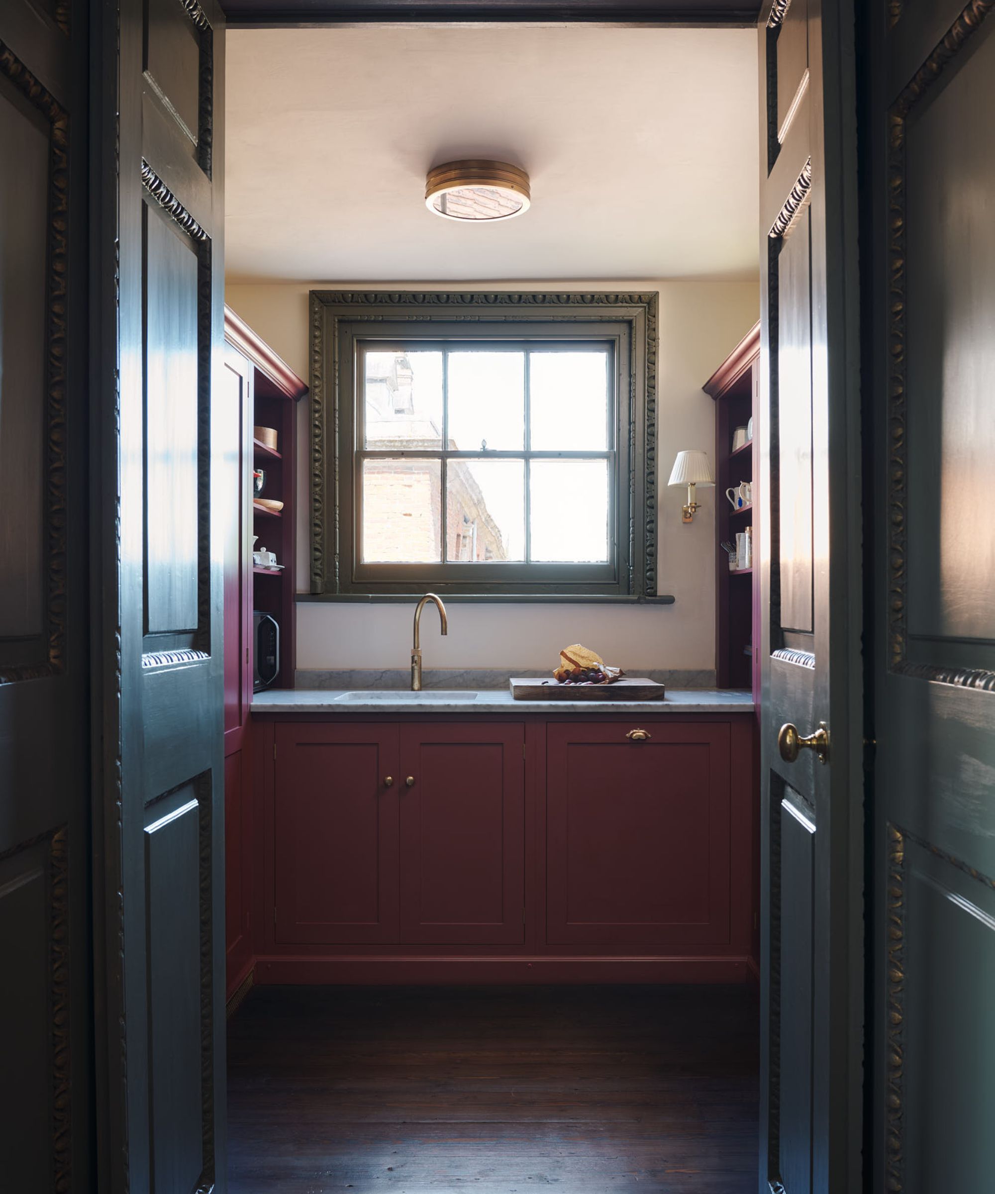 A stately pantry with red cabinets, white walls and a green window frame