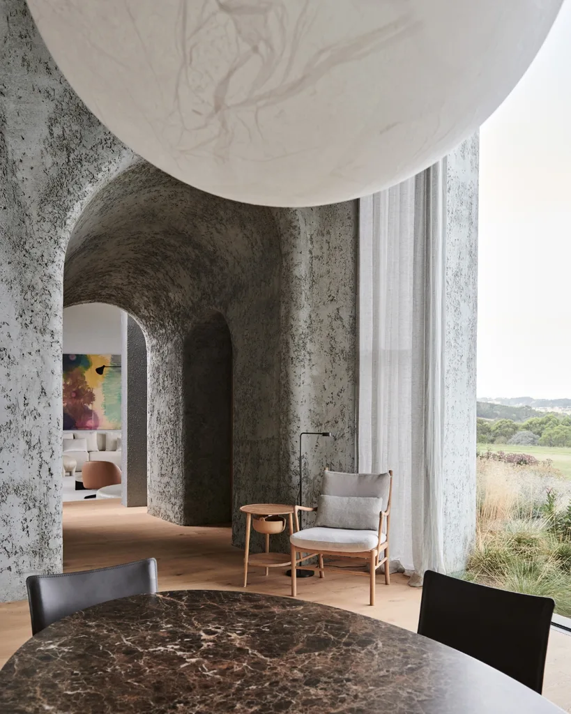 Concrete vaulted hallway with marble-dining table, white lantern and transparent curtains in front of the windows.