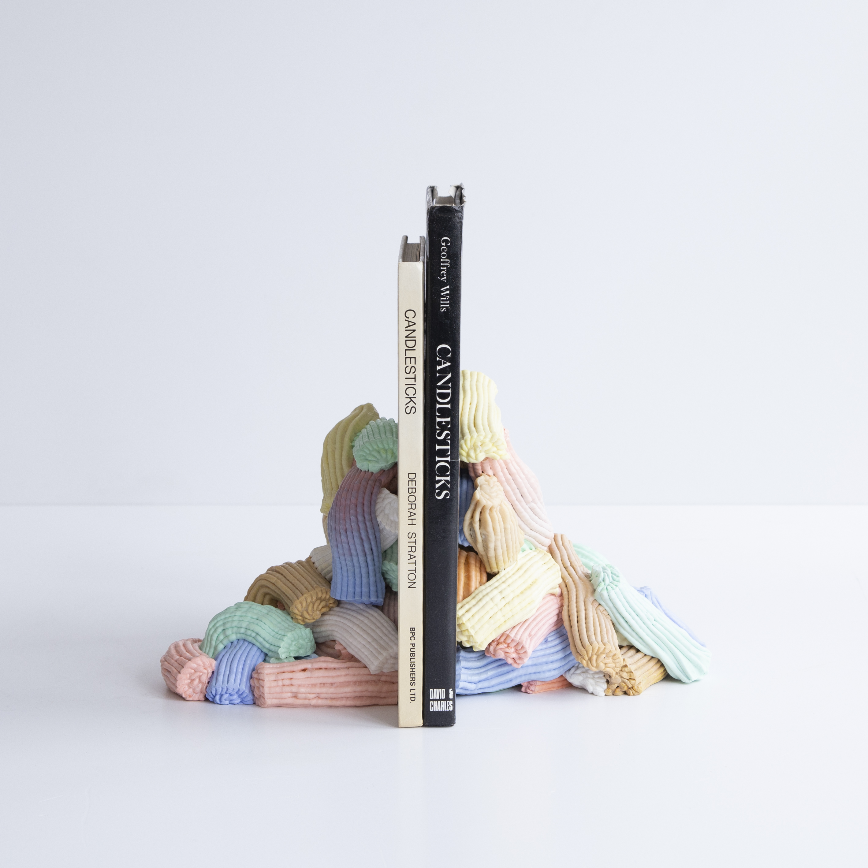 A book stand made of pastel, candy-colored material holds a beige and a black book in an all-white room.