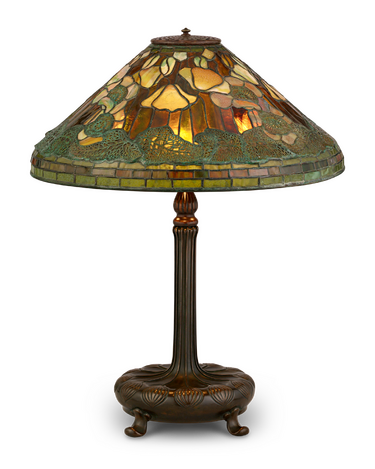 Vintage Tiffany style lamp with colorful stained glass shade and ornate bronze base, warmly lit against a dark background.
