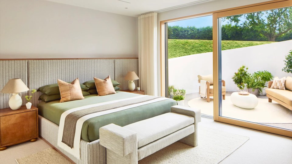 A bedroom with a green bedspread and orange pillows has a sliding glass door that leads to a patio.