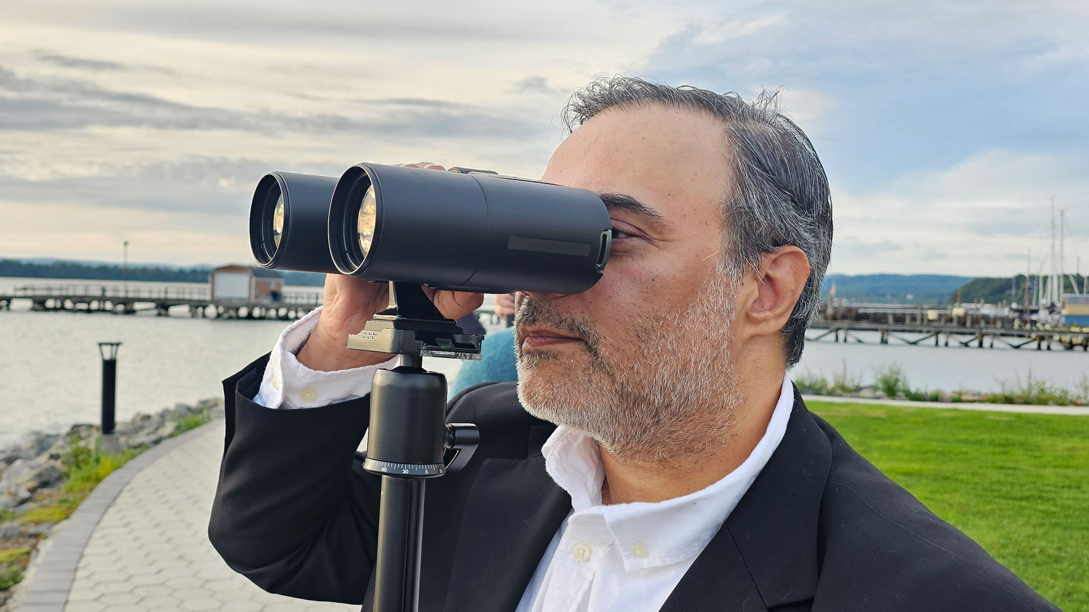 A man looks through Unistellar Envision smart binoculars with a dock in the background.