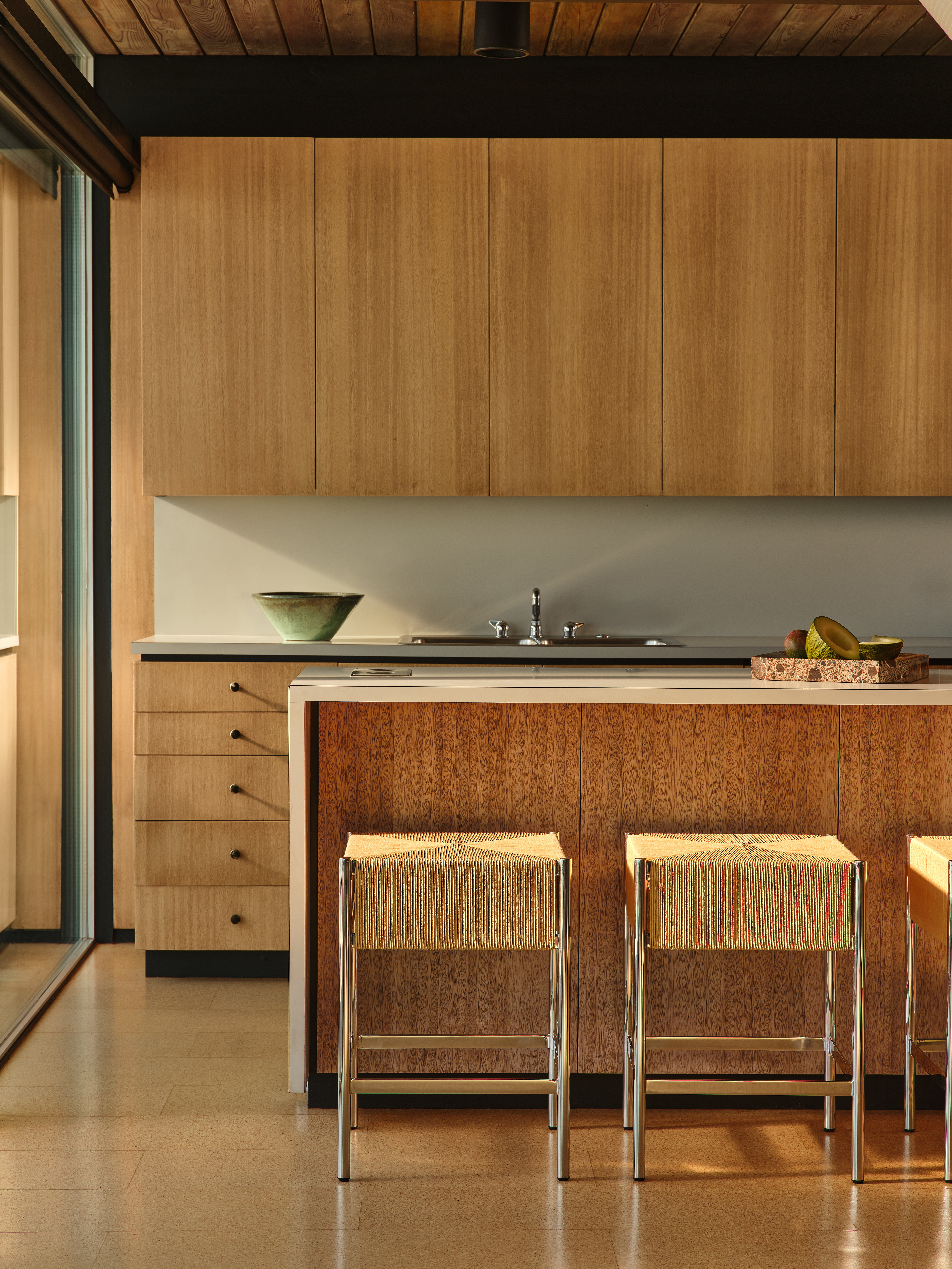 Corduroy stools stand in front of a kitchen island, warm wooden surfaces surround the room.
