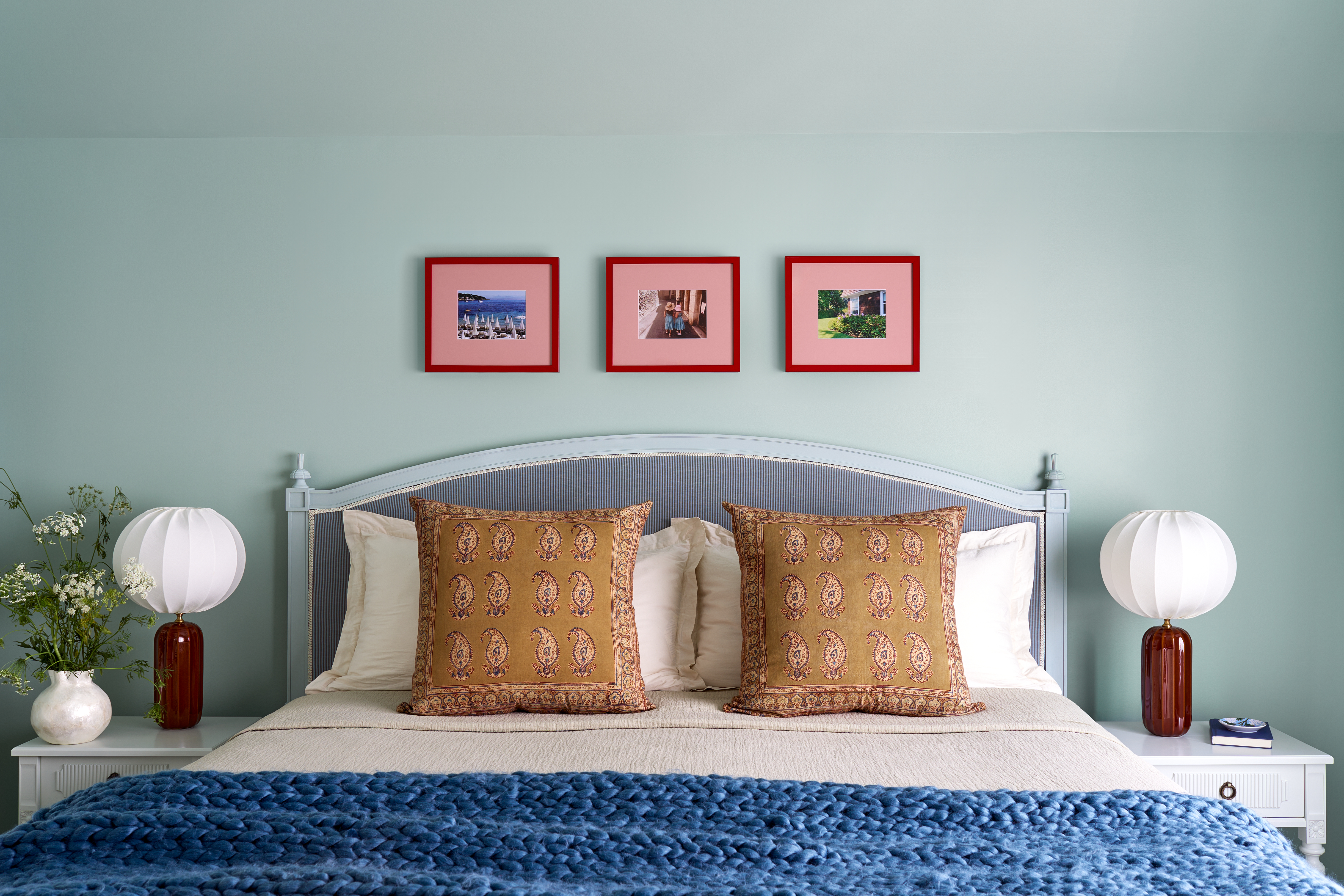 Three red and pink picture frames in a row form a gallery wall above a blue headboard.