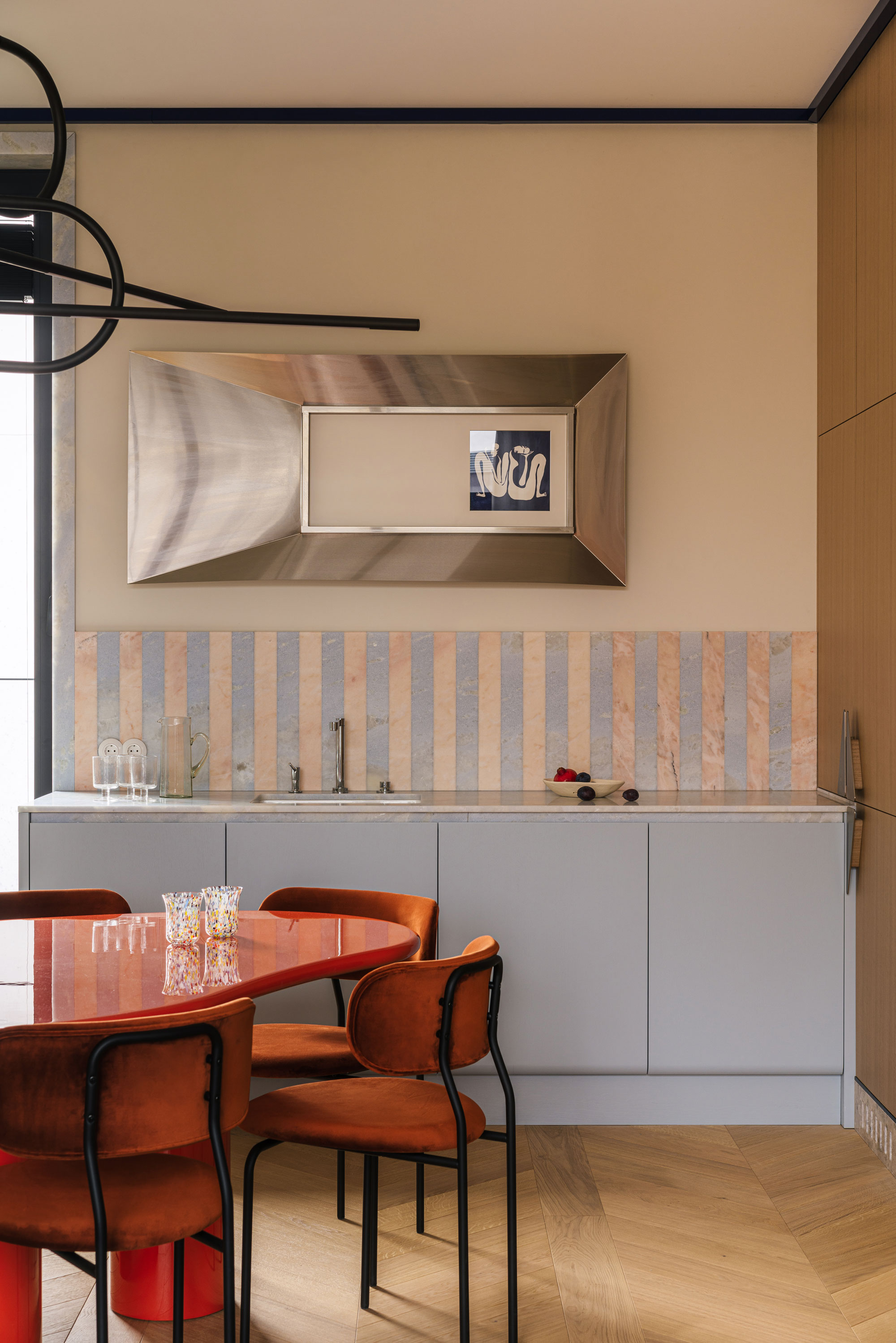 a light blue kitchen with a red table and chairs in front of it. A striped kitchen splashback hangs on the wall