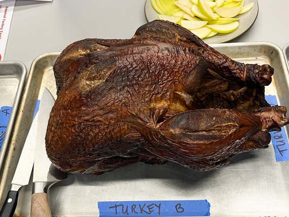 A whole, smoked turkey with dark, wrinkled skin sits on a labeled metal baking sheet "Türkiye B."